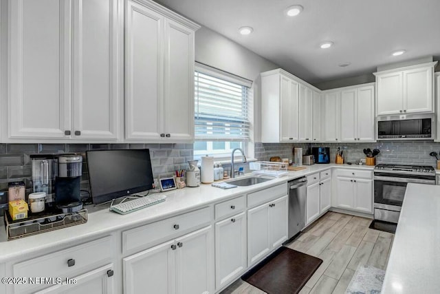 kitchen featuring light wood-style flooring, appliances with stainless steel finishes, light countertops, white cabinetry, and a sink