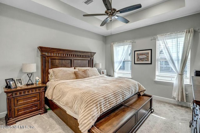 bedroom featuring a tray ceiling, light colored carpet, visible vents, a ceiling fan, and baseboards