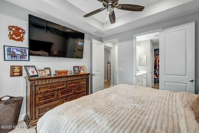 bedroom featuring baseboards, a closet, a walk in closet, a raised ceiling, and ensuite bath