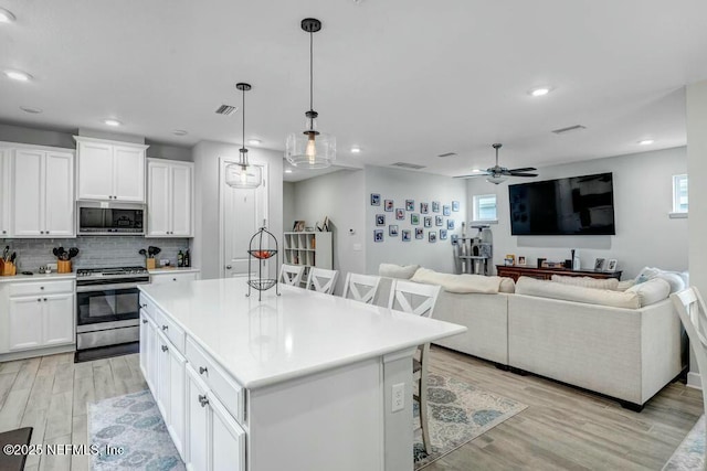 kitchen with stainless steel appliances, light wood-style floors, white cabinets, a kitchen breakfast bar, and tasteful backsplash