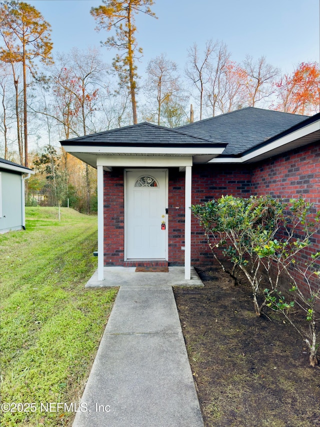 entrance to property with a yard, brick siding, and a shingled roof