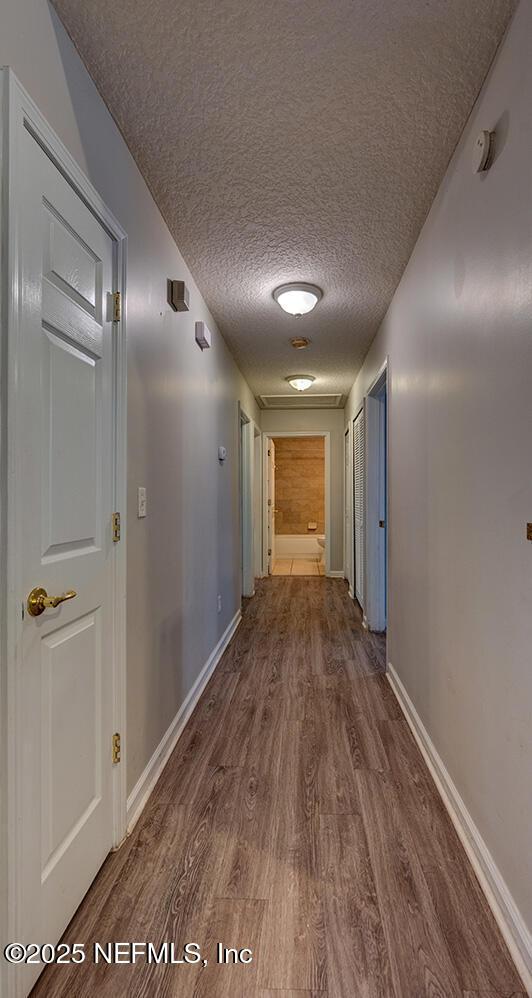 hall featuring a textured ceiling, baseboards, and wood finished floors