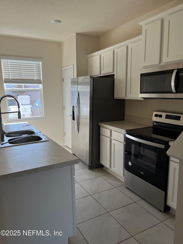 kitchen with white cabinets, light tile patterned floors, stainless steel appliances, and a sink