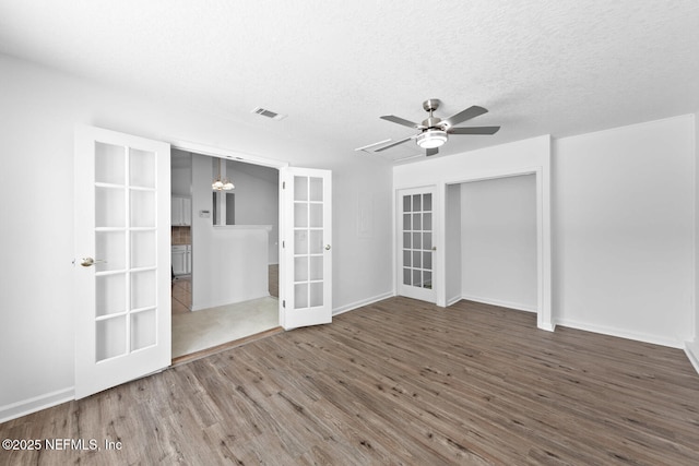 unfurnished bedroom with french doors, visible vents, a textured ceiling, wood finished floors, and baseboards