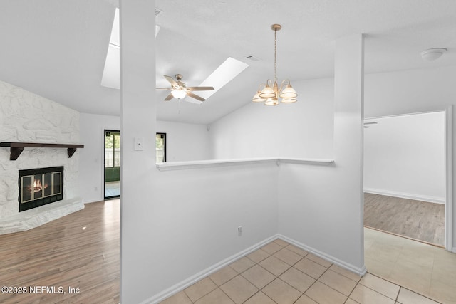 unfurnished room featuring lofted ceiling with skylight, wood finished floors, a fireplace, and ceiling fan with notable chandelier