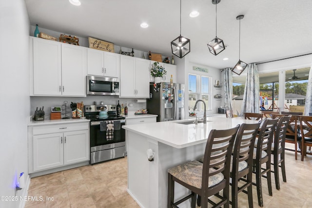 kitchen with decorative light fixtures, light countertops, appliances with stainless steel finishes, a sink, and an island with sink