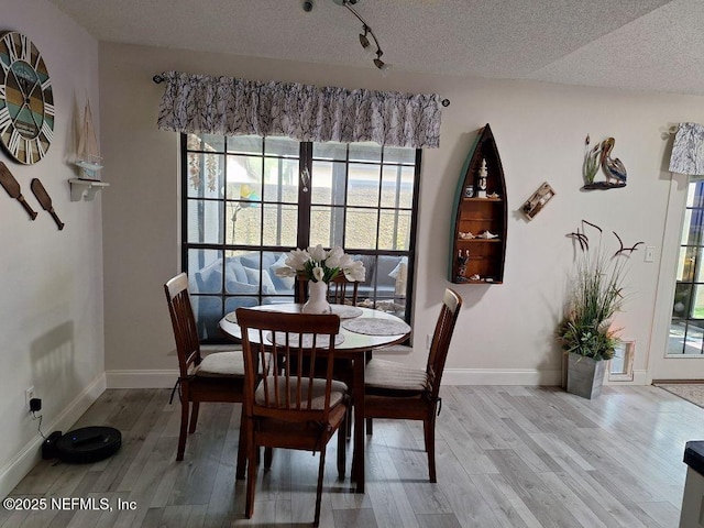 dining room featuring a textured ceiling, light wood-type flooring, and baseboards