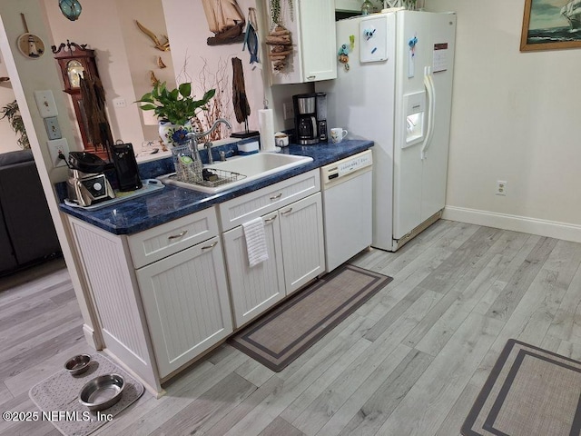 kitchen featuring dark countertops, white appliances, light wood-type flooring, and a sink