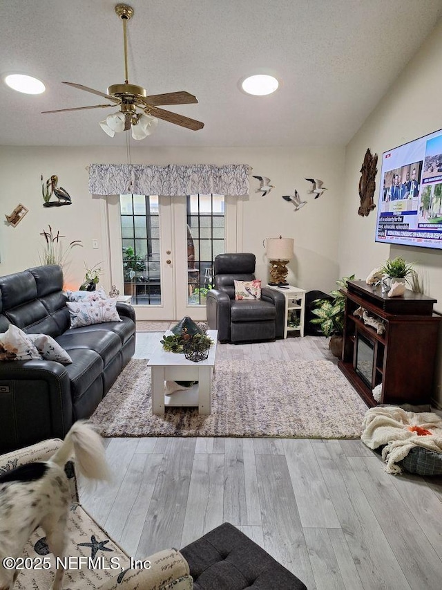 living area featuring french doors, a ceiling fan, vaulted ceiling, a textured ceiling, and wood finished floors