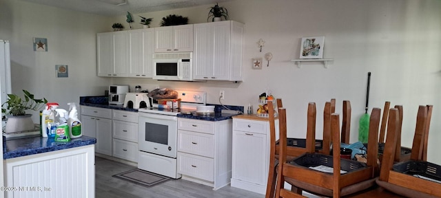 kitchen featuring dark countertops, white appliances, white cabinets, and wood finished floors