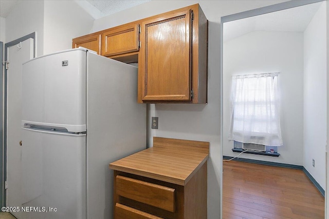 kitchen featuring hardwood / wood-style floors, lofted ceiling, freestanding refrigerator, light countertops, and brown cabinets