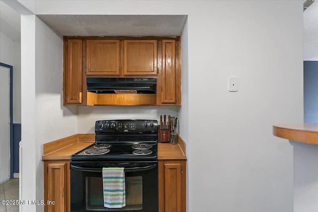 kitchen with black range with electric stovetop, under cabinet range hood, a textured ceiling, brown cabinetry, and light countertops