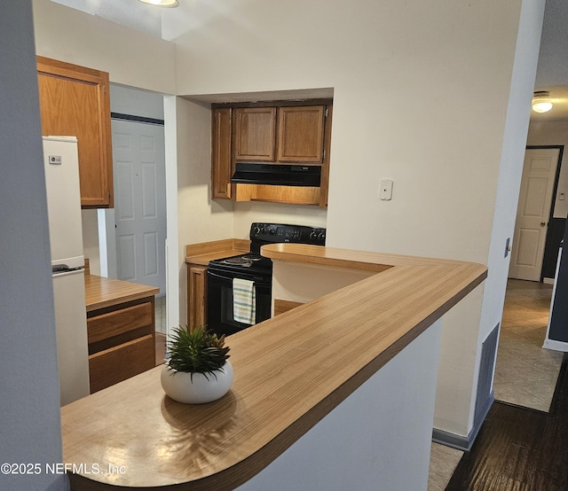 kitchen with butcher block countertops, black electric range, freestanding refrigerator, brown cabinetry, and extractor fan