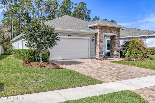 view of front of property featuring a garage, stone siding, roof with shingles, decorative driveway, and a front yard