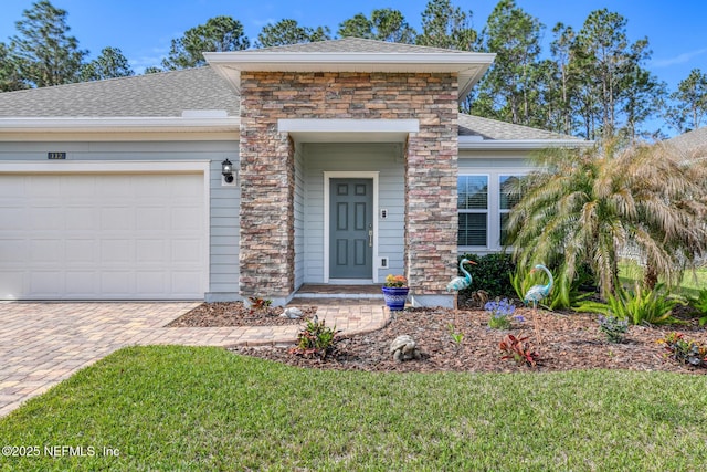 property entrance with a shingled roof, stone siding, an attached garage, decorative driveway, and a yard