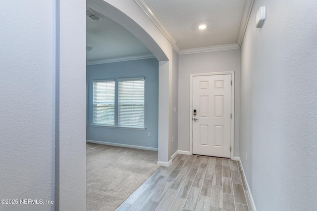 foyer entrance with arched walkways, wood finished floors, visible vents, baseboards, and ornamental molding