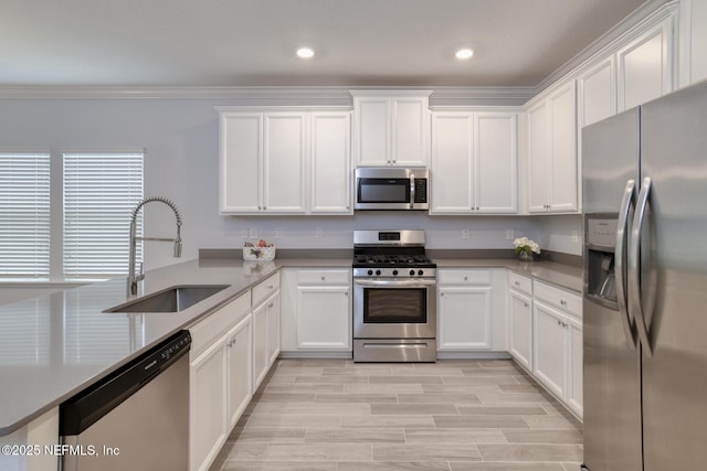 kitchen with white cabinets, appliances with stainless steel finishes, wood tiled floor, crown molding, and a sink