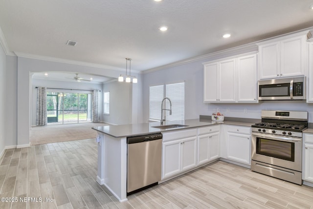 kitchen featuring appliances with stainless steel finishes, open floor plan, white cabinetry, a sink, and a peninsula