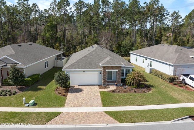 single story home with a garage, a shingled roof, brick siding, decorative driveway, and a front yard