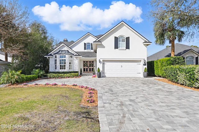 traditional-style home with stucco siding, decorative driveway, a front yard, an attached garage, and a chimney