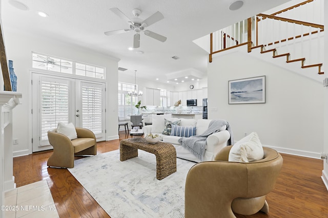 living room featuring ceiling fan with notable chandelier, stairs, light wood-type flooring, and baseboards