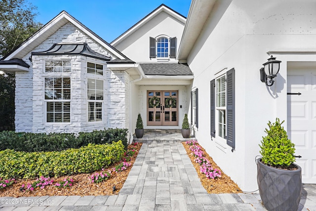 property entrance with stucco siding, stone siding, an attached garage, and french doors