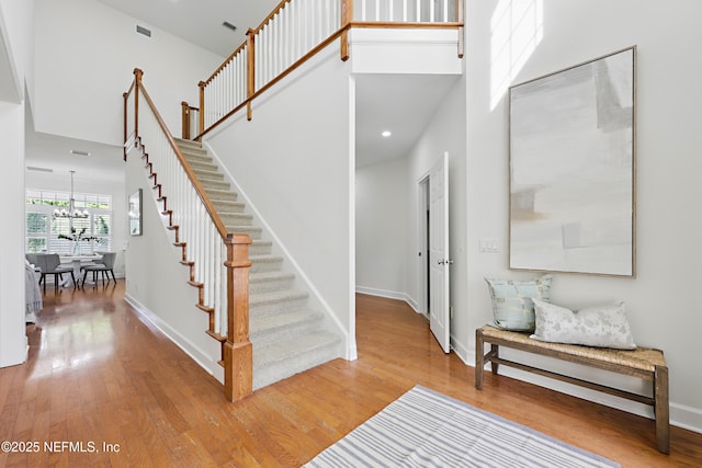 stairs with visible vents, baseboards, a towering ceiling, and wood finished floors