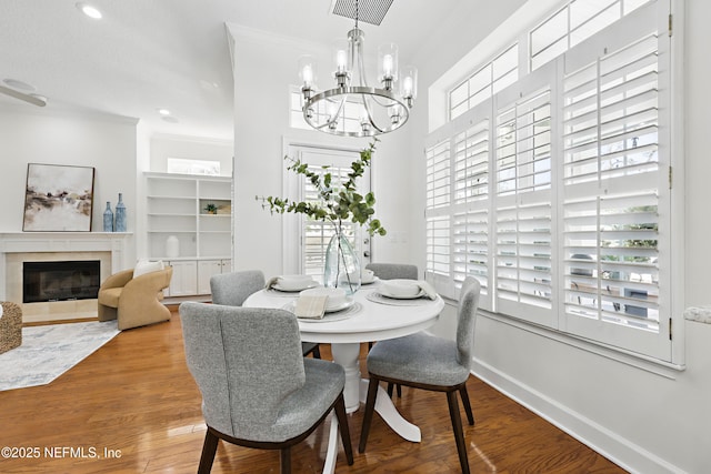 dining room with a glass covered fireplace, wood finished floors, an inviting chandelier, crown molding, and baseboards