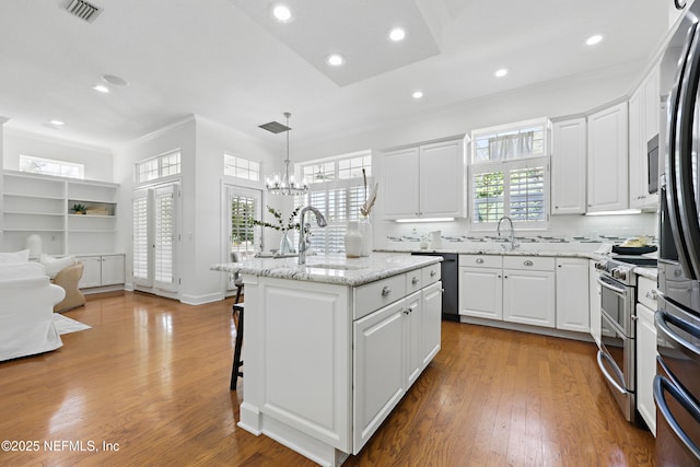 kitchen featuring visible vents, ornamental molding, appliances with stainless steel finishes, wood finished floors, and a sink