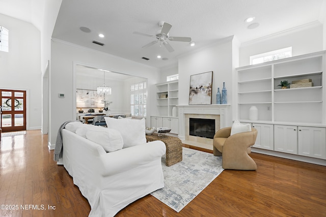 living area featuring visible vents, dark wood finished floors, crown molding, and ceiling fan with notable chandelier