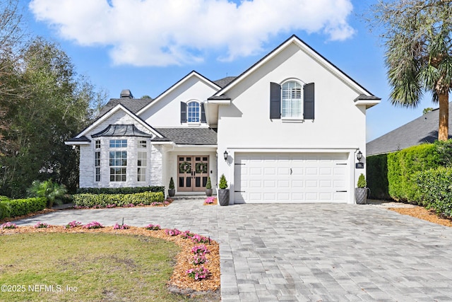 view of front of house with roof with shingles, stucco siding, french doors, a garage, and decorative driveway