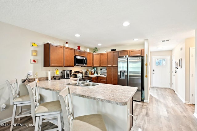 kitchen with appliances with stainless steel finishes, brown cabinets, light countertops, and a peninsula