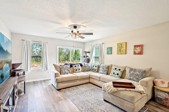 living room with ceiling fan, a textured ceiling, baseboards, and wood finished floors