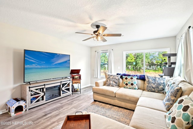 living area with a ceiling fan, a textured ceiling, baseboards, and wood finished floors