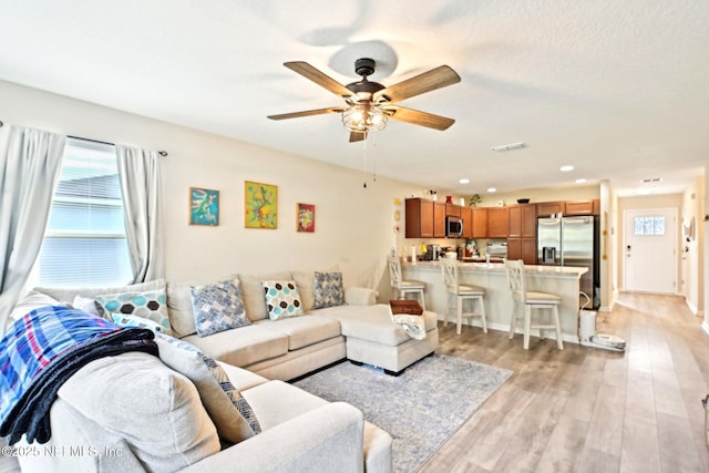 living area featuring light wood finished floors, ceiling fan, and visible vents