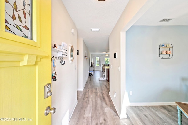 hall featuring wood finished floors, visible vents, and baseboards