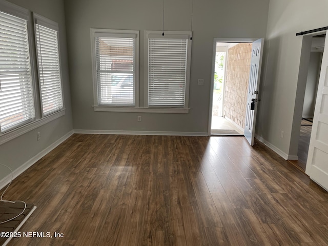 interior space with dark wood finished floors, a barn door, and baseboards