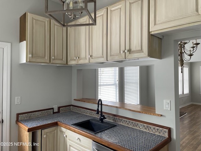 kitchen with cream cabinetry, a sink, dark countertops, wood finished floors, and dishwasher