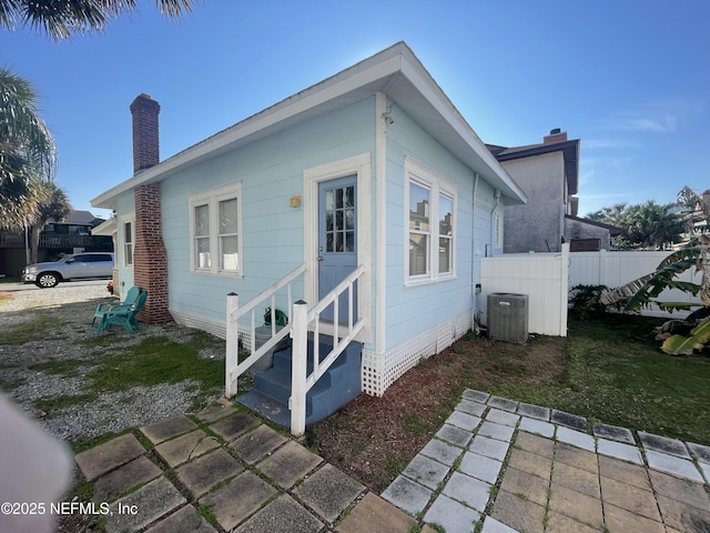 view of home's exterior with central air condition unit, entry steps, a chimney, and fence