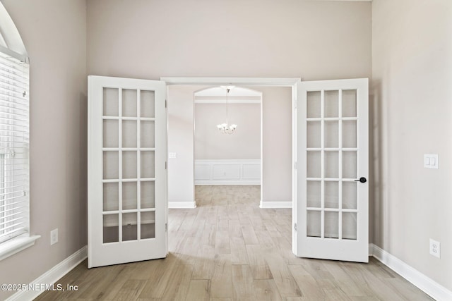 spare room featuring baseboards, french doors, wood finished floors, and an inviting chandelier