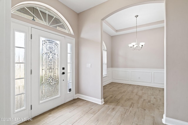 foyer entrance featuring arched walkways, a decorative wall, light wood-style floors, wainscoting, and a chandelier