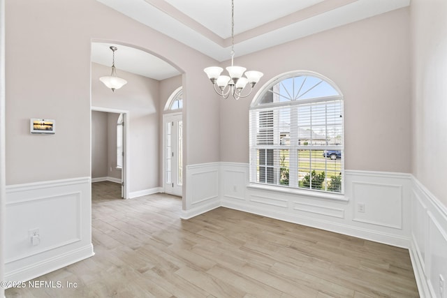 empty room with light wood finished floors, a chandelier, and wainscoting