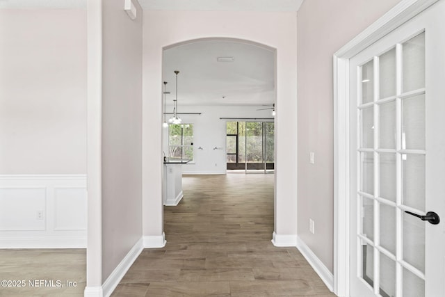 corridor featuring arched walkways, wood finished floors, and baseboards