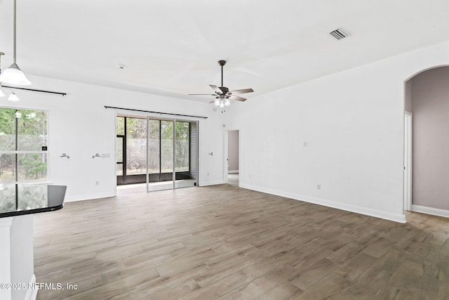 interior space with arched walkways, visible vents, light wood-style flooring, ceiling fan, and baseboards