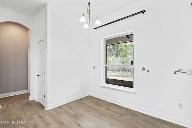 unfurnished dining area with arched walkways, wood finished floors, and baseboards