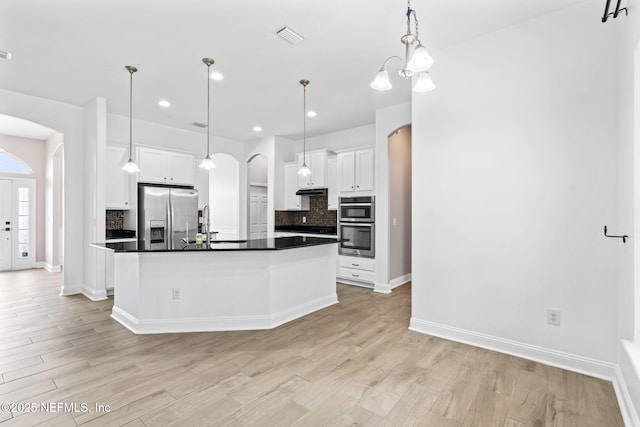 kitchen with light wood finished floors, arched walkways, stainless steel appliances, and decorative backsplash