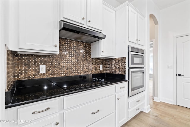 kitchen with arched walkways, black electric cooktop, under cabinet range hood, double oven, and backsplash