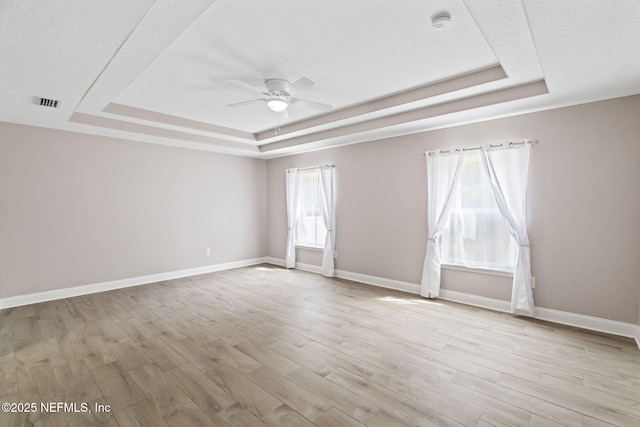 empty room featuring plenty of natural light, a tray ceiling, and wood finished floors