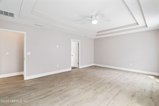 unfurnished room featuring a tray ceiling, light wood finished floors, visible vents, a ceiling fan, and baseboards