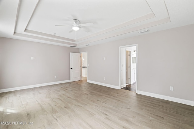 spare room featuring a tray ceiling, visible vents, light wood-style flooring, a ceiling fan, and baseboards